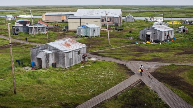 People walk down the elevated, raised wooden sidewalks—created so people don't sink into the melting permafrost—on July 5th, 2015, in Newtok, Alaska. Newtok, which is having to relocate due to melting permafrost and rapid erosion of the river it is established next to, has to have all its fuel and fresh water brought in aboard tankers.