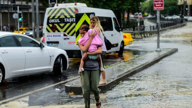 A woman carrying a baby crosses a street during a heavy downpour of rain at Taksim in Istanbul on July 27th, 2017.