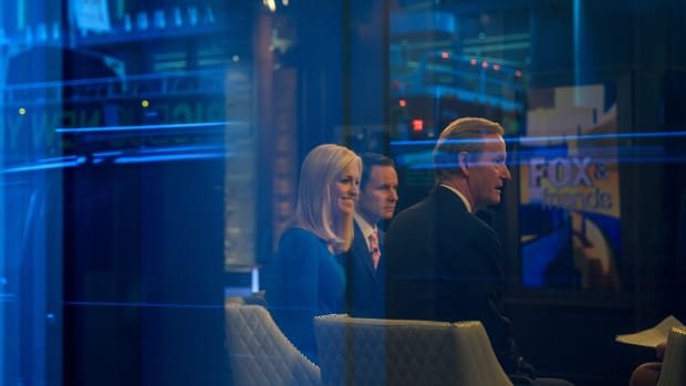Seen through a window, (from left) hosts Ainsley Earhardt, Brian Kilmeade, and Steve Doocy broadcast Fox and Friends from the Fox News studios on February 17th, 2017, in New York City.