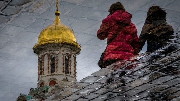 Women are reflected in a puddle as they walk across the Red Square in Moscow on April 26th, 2018.