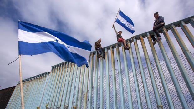 People hold Honduran flags at the border fence during a rally with members of a caravan of Central American asylum seekers and supporters on April 29th, 2018, in Tijuana, Mexico.