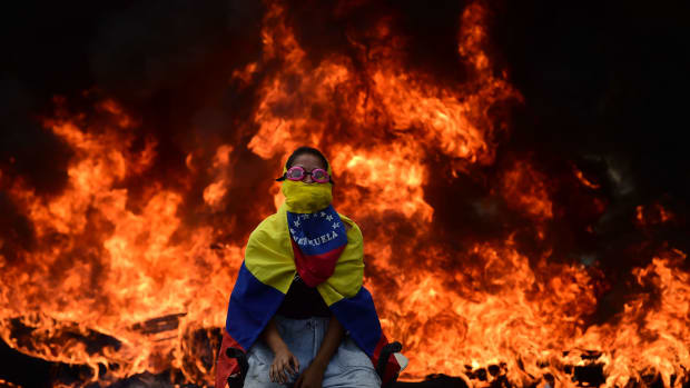 A Venezuelan opposition activist is backdropped by a burning barricade during a demonstration against President Nicolas Maduro in Caracas, on April 24th, 2017. Protesters rallied on Monday vowing to block Venezuela's main roads to raise pressure on Maduro after three weeks of deadly unrest that have left 21 people dead. Riot police fired rubber bullets and tear gas to break up one of the first rallies in eastern Caracas early Monday while other groups were gathering elsewhere, the opposition said.
