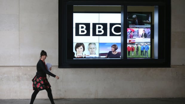 A woman walks past a bank of television screens displaying BBC channels in the BBC headquarters on November 12th, 2012, in London, England.