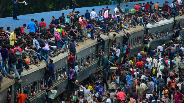 People scramble to reach the roof of an overcrowded train at a station in Dhaka, Bangladesh, on August 20th, 2018. Crowds rushed home from the capital city to be with friends and family during the annual holiday of Eid al-Adha, also known as the Festival of Sacrifice, celebrated by Muslims worldwide.