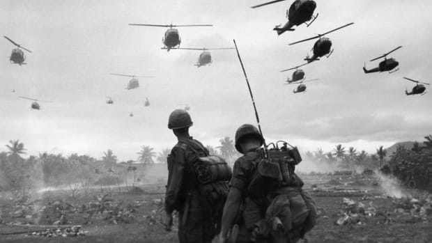 The second wave of combat helicopters of the 1st Air Cavalry Division fly over an RTO and his commander on an isolated landing zone during Operation Pershing, a search and destroy mission on the Bong Son Plain and An Lao Valley of South Vietnam, during the Vietnam War.