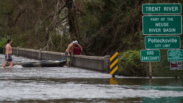 Two men pulling a kayak pick up a gas canister as they walk across a road flooded by Hurricane Florence in Pollocksville, North Carolina, on September 16th, 2018.