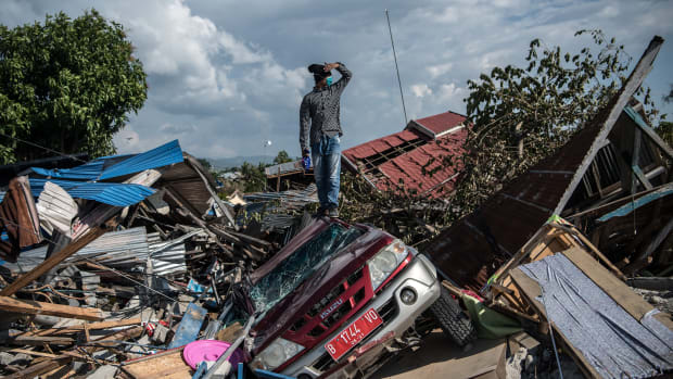 A man stands on a destroyed car as he views the rubble and debris of destroyed buildings following an earthquake, on October 2nd, 2018, in Palu, Indonesia.