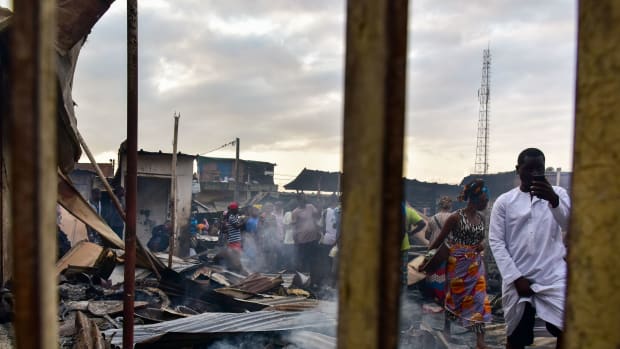 A man takes photos with a mobile phone as sellers walk through debris in a market after a fire devastated the building overnight on September 18th, 2017, in the Abobo neighborhood of Abidjan.