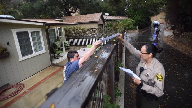 A Los Angeles County sheriff's deputy alerts a resident of mandatory evacuations on January 8th, 2018, in the Creek Fire burn area.