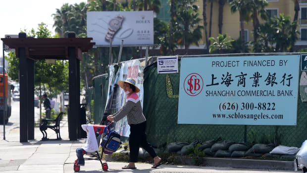 A woman pushes a stroller in San Gabriel, California, on May 17th, 2016, past a banner at a construction site project financed by the Shanghai Commercial Bank.