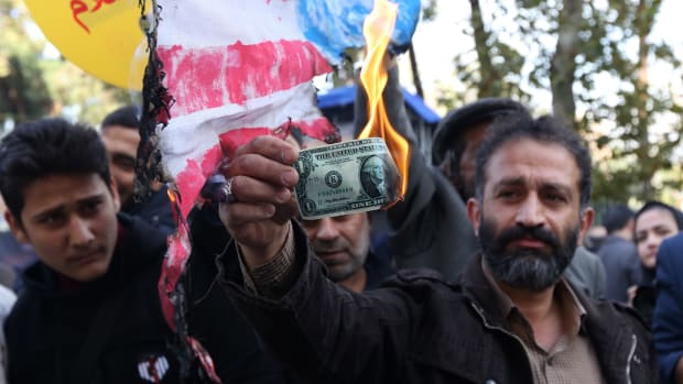 On the eve of renewed sanctions by Washington, An Iranian protester burns a dollar banknote during a demonstration outside the former U.S. embassy in the Iranian capital of Tehran.