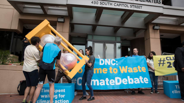 A group of people flip over an hourglass in front of the Democratic National Committee headquarters during a Green Peace rally to call for a presidential climate debate on June 12th, 2019, in Washington, D.C.