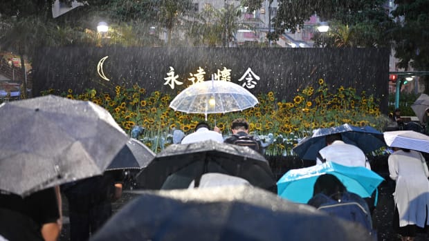 People bow to pay their respects after leaving sunflowers on a stage, as they attend a memorial event during heavy rainfall in Hong Kong on July 11th, 2019.