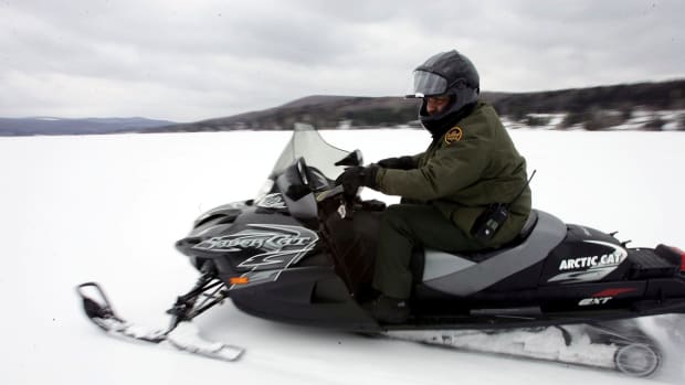 A U.S. Border Patrol Agent rides a snowmobile during a patrol on a frozen lake that splits the Canadian territory behind him and the U.S., near Norton, Vermont.