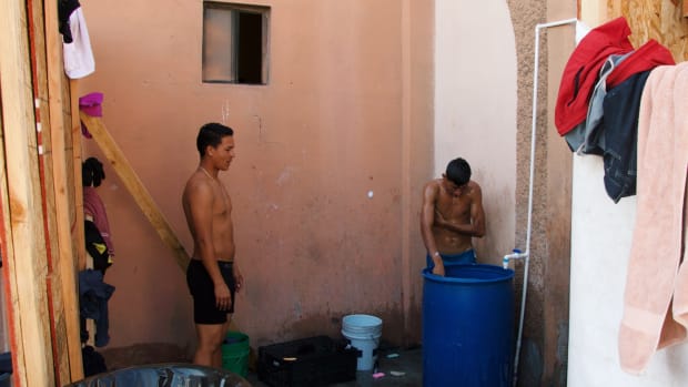 Two migrants wash in the rudimentary bathing area inside the pavilion for children and families.