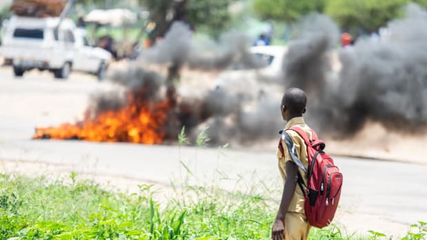 A school boy looks at a burning barricade during a demonstration on January 14th, 2019, in Bulawayo, Zimbabwe. Angry protesters barricaded roads with burning tires and rocks after the government more than doubled the price of fuel in a bid to improve supplies as the country battles its worst gasoline shortage in a decade.