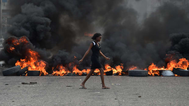 A woman walks past tire barricades set ablaze by demonstrators on February 10th, 2019, the fourth day of protests in Port-au-Prince.