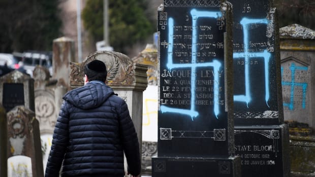 A man walks by graves vandalized with swastikas at the Jewish cemetery in Quatzenheim, France, on February 19th, 2019, the day of a nationwide march against a rise in anti-Semitic attacks. Around 80 graves have been vandalized at the Jewish cemetery in the village, close to the border with Germany in the Alsace region. The graffiti was discovered early Tuesday, according to a statement from the regional security office.