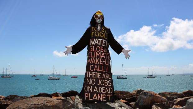 Benny Zable, a performance artist for peace and environment, stands in costume at the edge of Airlie Bay during an anti-Adani Carmichael coal mine rally on April 26th, 2019, in Airlie Beach, Australia.