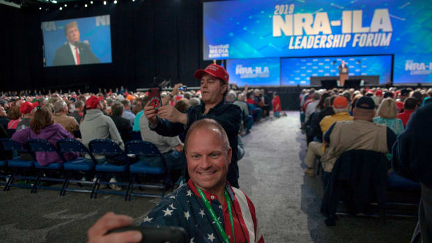 Skippy Thomas, a member of the National Rifle Association, takes a selfie with President Donald Trump in the background during the NRA's annual meeting at Lucas Oil Stadium in Indianapolis, Indiana, on April 26th, 2019.