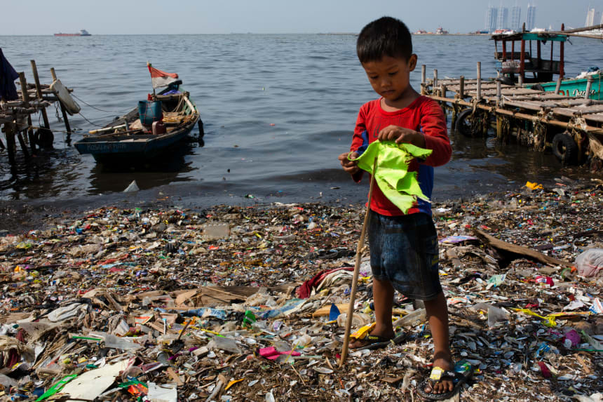 A boy plays with a makeshift flagpole on a beach covered in plastic waste at a fishing village on the northern coast on May 31st, 2018, in Jakarta, Indonesia.  Indonesia has been ranked the second largest marine polluter in the world behind only China, with reports showing that the country produces 187.2 million tons of plastic waste each year.