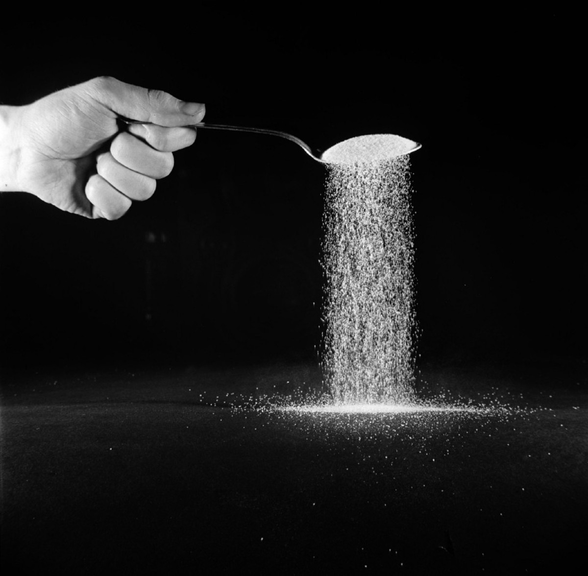 Photo of a person's hand, holding a spoonful of sugar