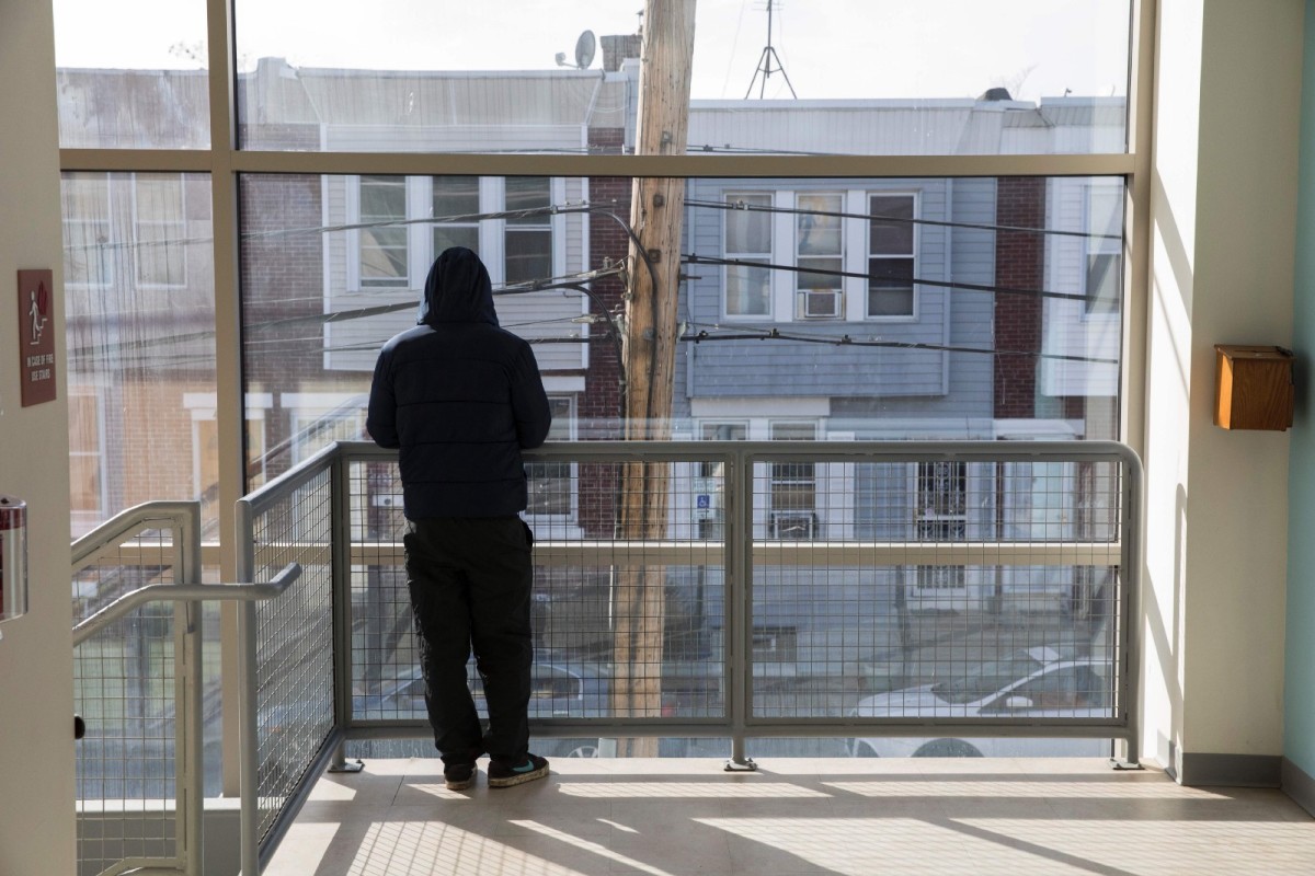 A man stands at a window looking out over North Philadelphia.