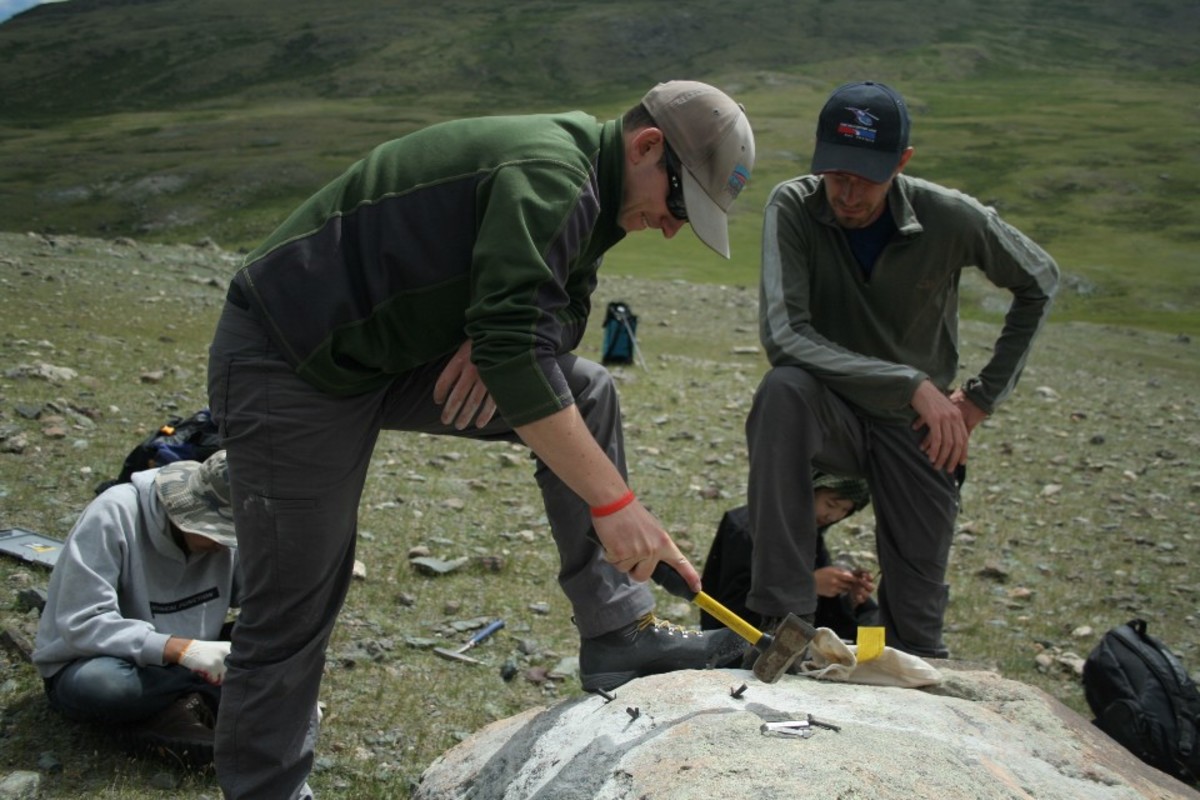 Peter Strand, tapping metal shims into the rock; after drilling, Strand cleans its surface.