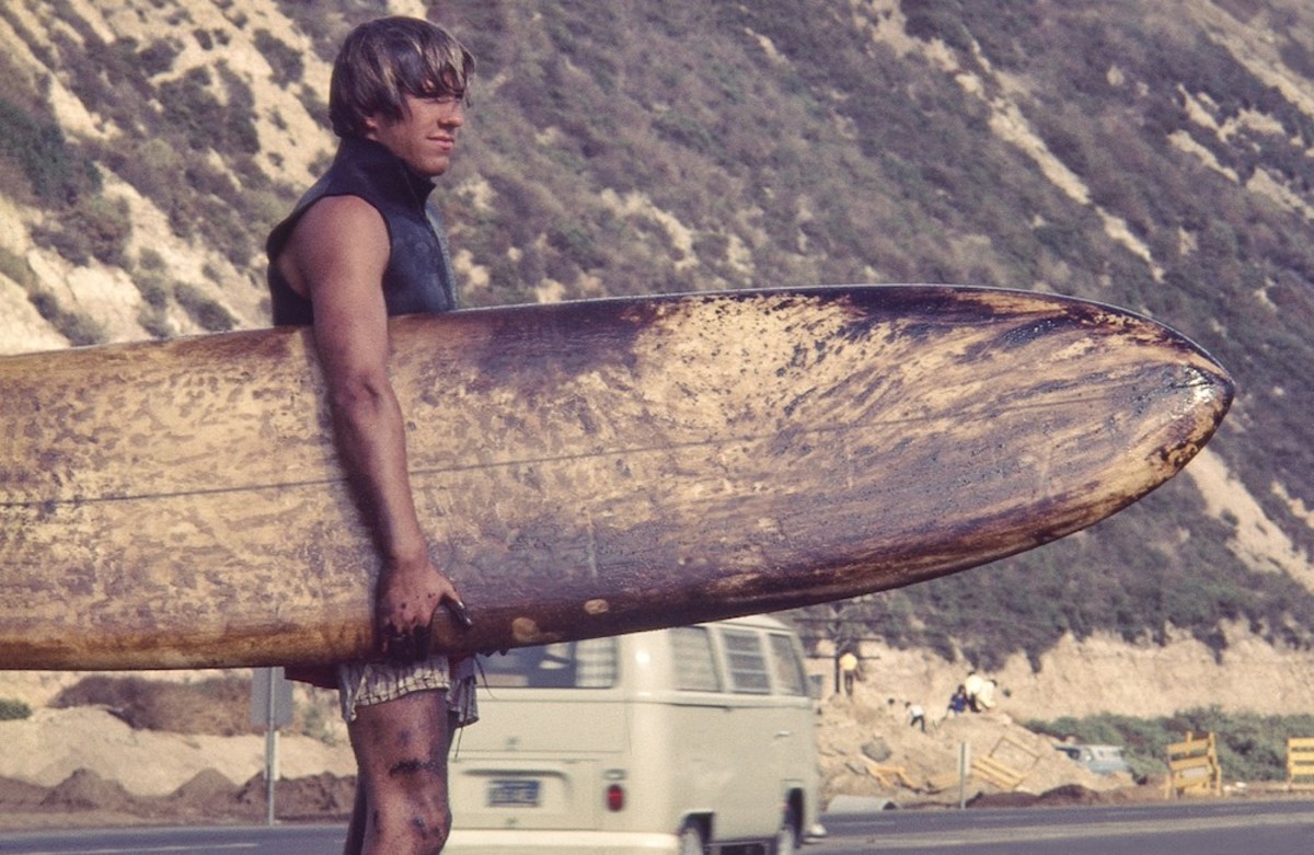 A surfer carries his oil-coated board.