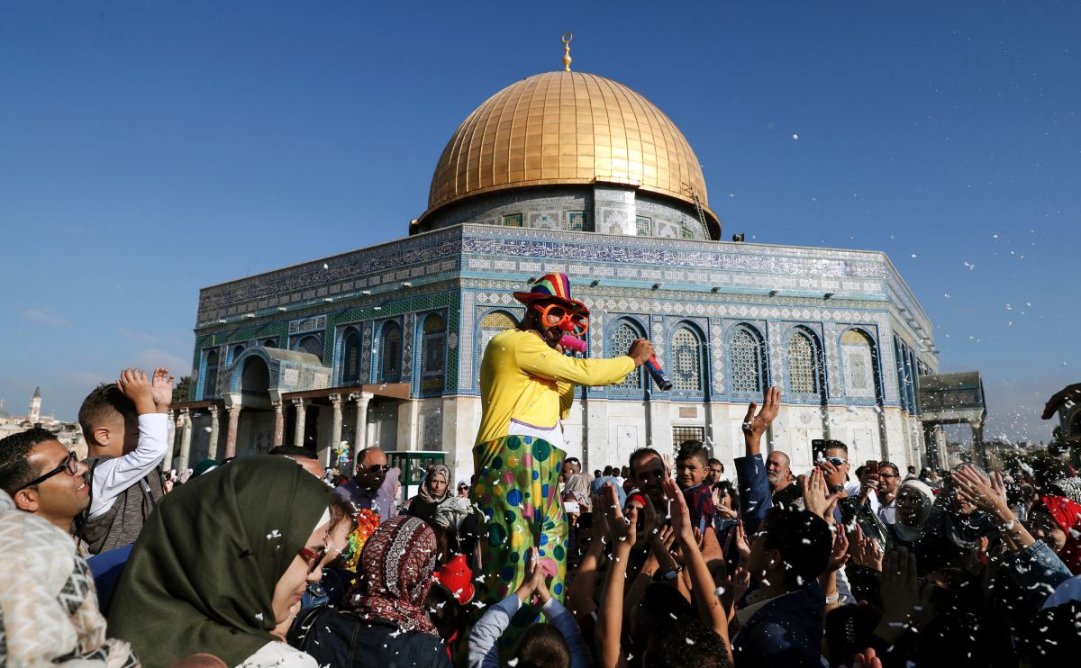 A man dressed in a clown outfit distributes balloons to children as confetti is thrown by the Dome of the Rock inside al-Aqsa Mosque compound, in Jerusalem's old city on the first day of Eid al-Adha on September 1st, 2017.