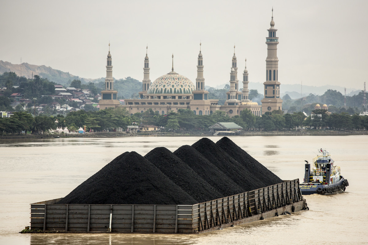 A tug pulls a coal barge past the Islamic centre on August 26th, 2016, in Samarinda, Kalimantan, Indonesia.