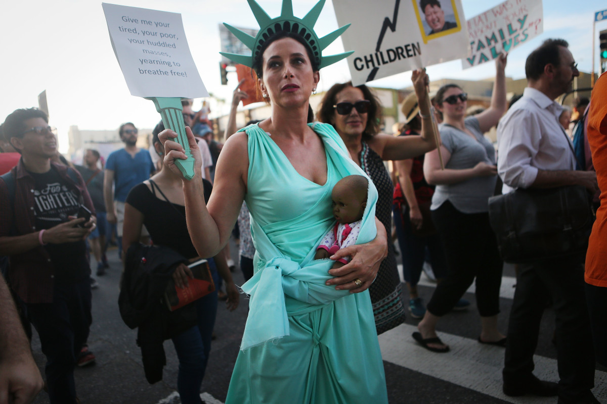 A protester dressed as Lady Liberty carries a doll, depicting a baby of color, as demonstrators march at the "Families Belong Together" march against the separation of children of immigrants from their families on June 14th, 2018, in Los Angeles, California. Demonstrators marched through the city and culminated the march at a detention center where ICE detainees are held.