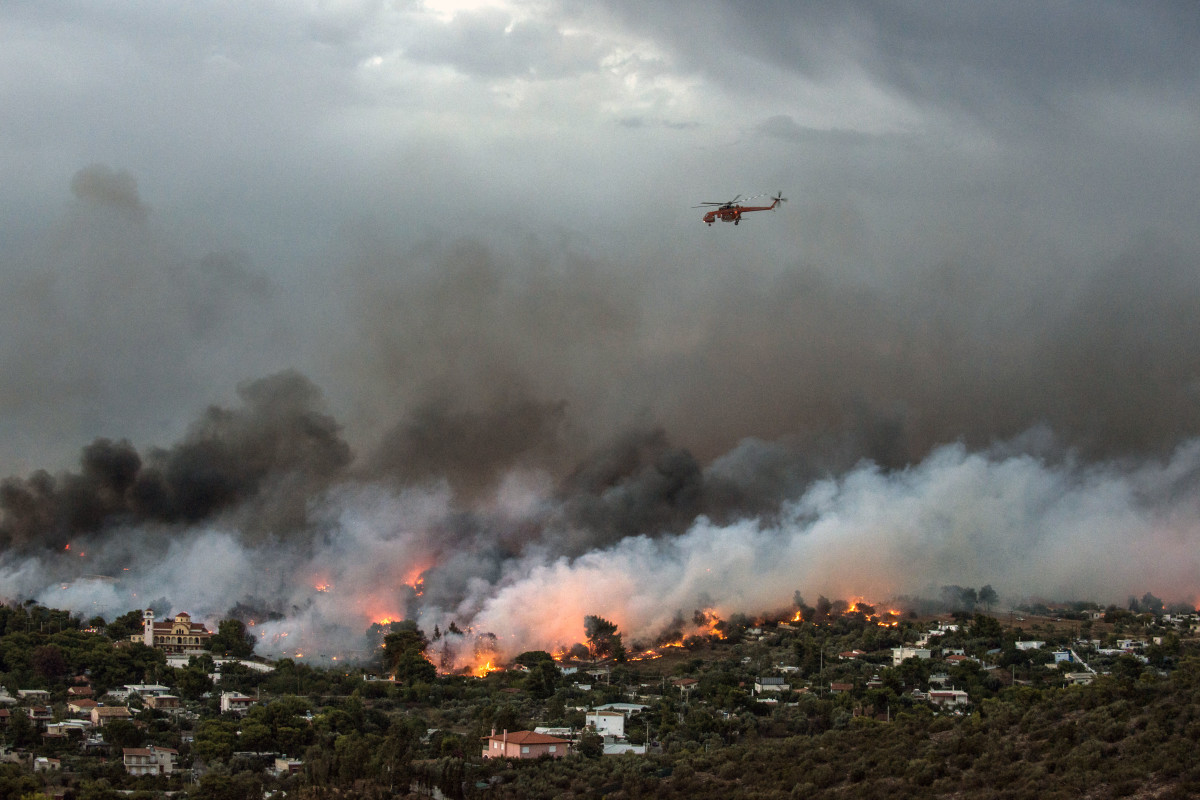 A firefighting helicopter flies over a wildfire raging in the town of Rafina near Athens, on July 23rd, 2018. At least five people have died and more than 20 have been injured as wildfires tore through woodland and villages around Athens on Monday, while blazes caused widespread damage in Sweden and other northern European nations.