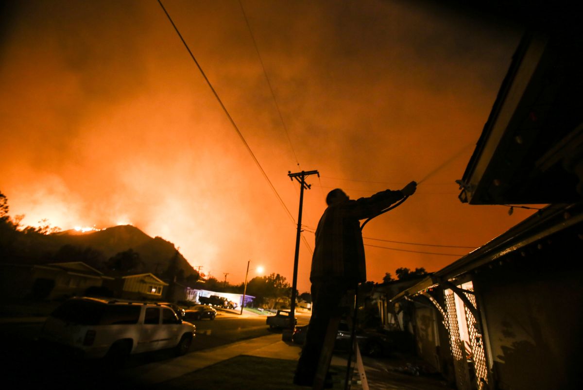 A man waters his home as firefighters battle the Thomas fire along a hillside near homes in Santa Paula, California, on December 5th, 2017.