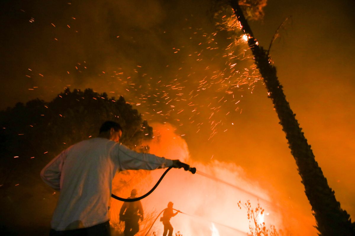 A man waters his home as firefighters battle a wildfire as it burns along a hillside near homes in Santa Paula, California.