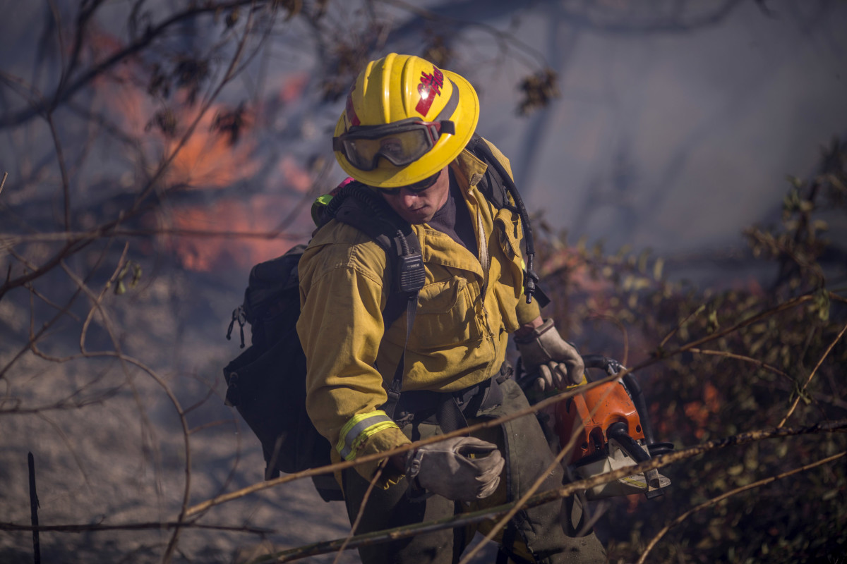 A firefighter cuts brush at the Thomas Fire on December 7th, 2017, near Fillmore, California. Strong Santa Ana winds are pushing multiple wildfires across the region, expanding across tens of thousands of acres and destroying hundreds of homes and structures.