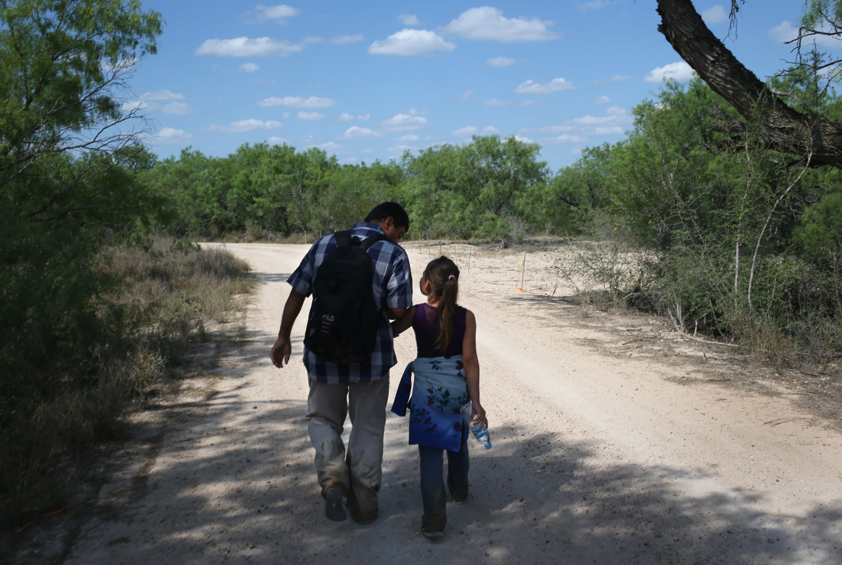 A father and his daughter walk through the South Texas countryside after crossing the Rio Grande from Mexico into the United States to seek asylum on April 14th, 2016, in Roma, Texas.