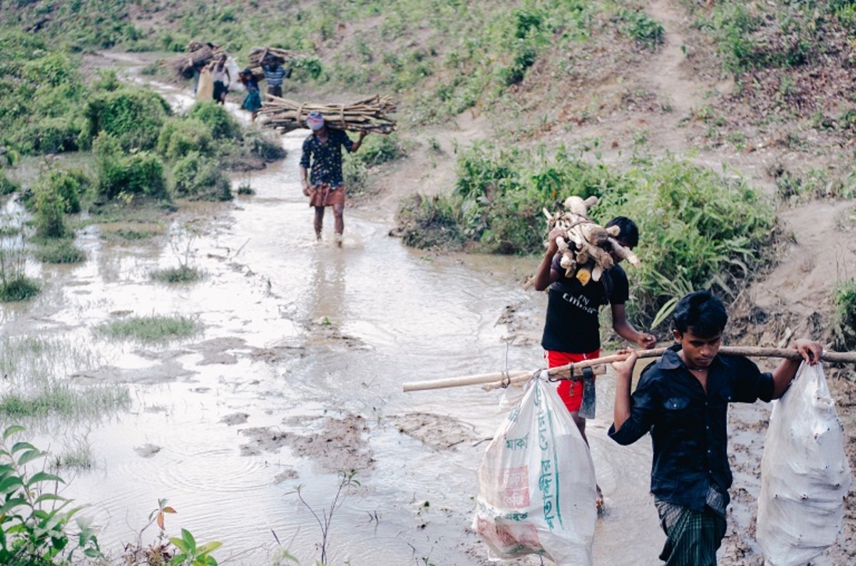 Rohingya men wade through water after heavy rains while returning from collecting firewood.