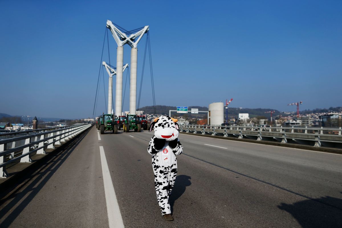 A person in a cow costume walks near farmers in their tractors, which block Gustave-Flaubert Bridge in Rouen, France, during a demonstration on February 21st, 2018, to protest against the trade deal negotiations in Brussels between Mercosur and the European Union. The negotiations include a revision of the map of disadvantaged areas through which certain communes receive aid.