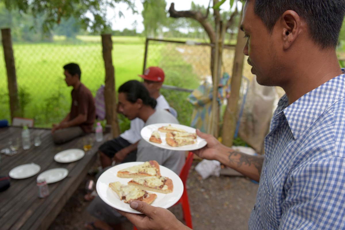 Nheb Thai, a Cambodian refugee who was deported from the U.S., carries plates with pizza as he serves a meal to a group of other deportees in Cambodia.