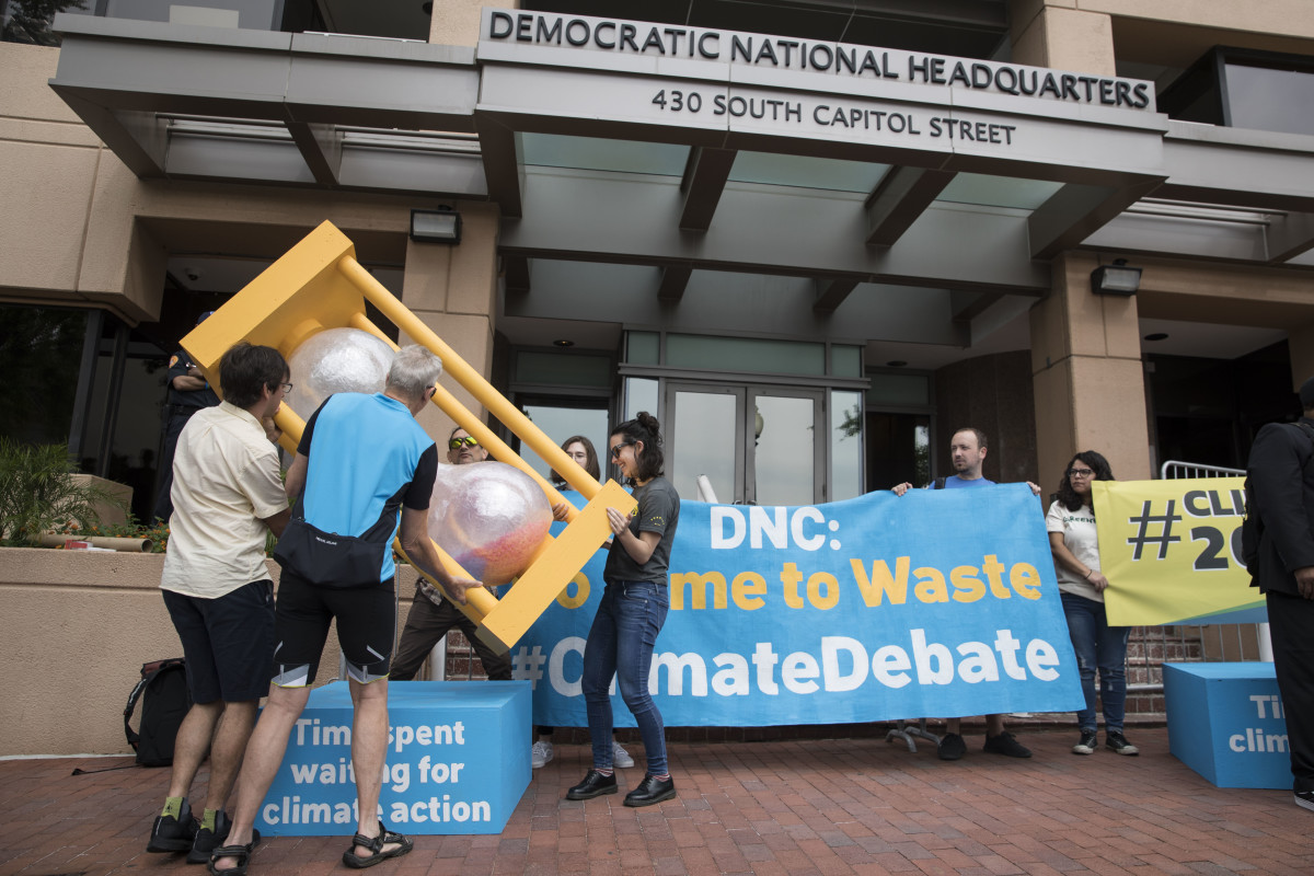 A group of people flip over an hourglass in front of the Democratic National Committee headquarters during a Green Peace rally to call for a presidential climate debate on June 12th, 2019, in Washington, D.C.