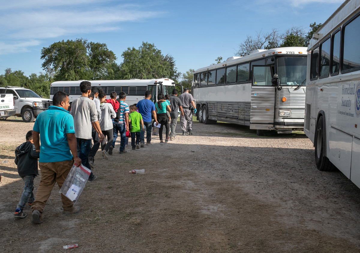Immigrants walk to U.S. Homeland Security buses to be transferred to a U.S. Border Patrol facility in McAllen after crossing from Mexico on July 2nd, 2019, in Los Ebanos, Texas.