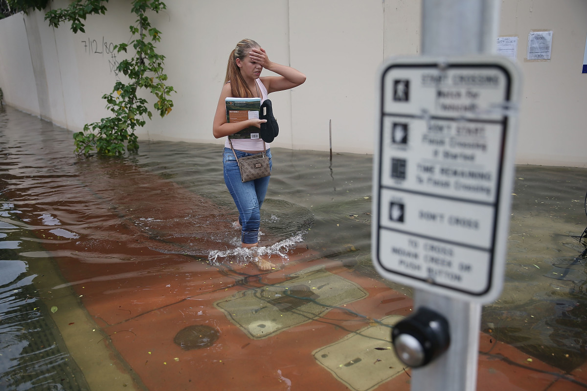 A woman walks through a flooded street that was caused by high tides and sea level rise due to climate change on September 29th, 2015, in Miami Beach, Florida.
