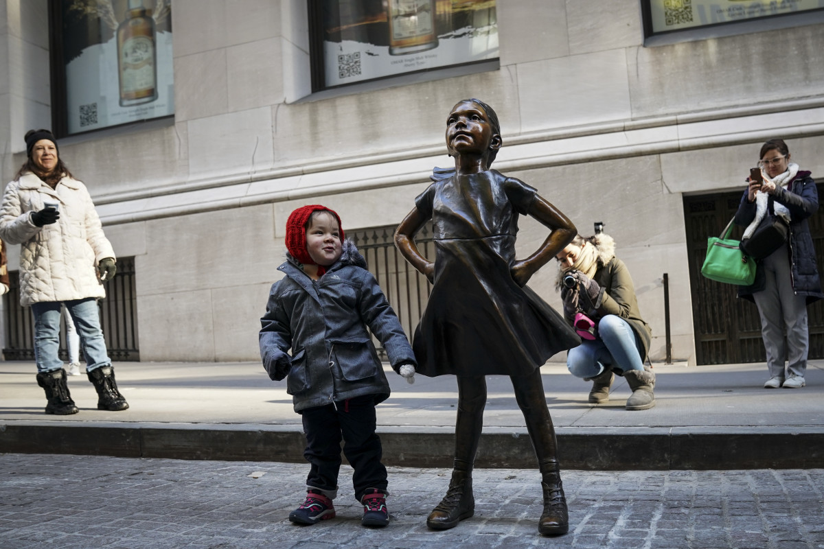A child stands alongside the Fearless Girl after a ceremony unveiling the statue's new permanent location outside the New York Stock Exchange on December 10th, 2018. The bronze statue, symbolizing female empowerment, has been moved from its Wall Street home opposite the Charging Bull statue in New York City.