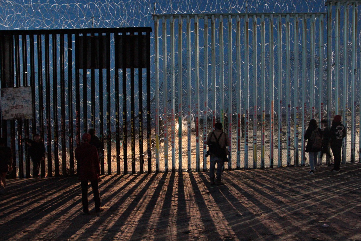 Border Patrol agents shine a light through the border wall as migrants search for a way to cross.