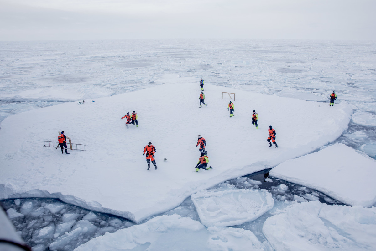 The crew of patrol vessel KV Svalbard and scientists from the Norwegian Institute of Marine Research play football on a floe of offshore ice on March 22nd, 2018, in the sea around Greenland, while two armed guards keep watch for polar bears.