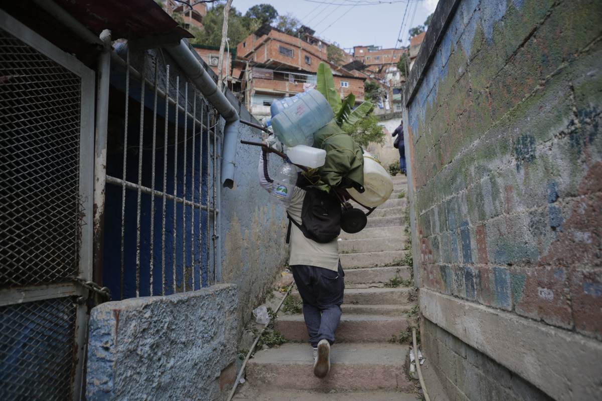 Eduardo Romero, a barber and pastry cook, leaves his parents' house carrying empty containers that he will fill with water at his home, at the slum of Petare, on April 4th, 2019, in Caracas, Venezuela.