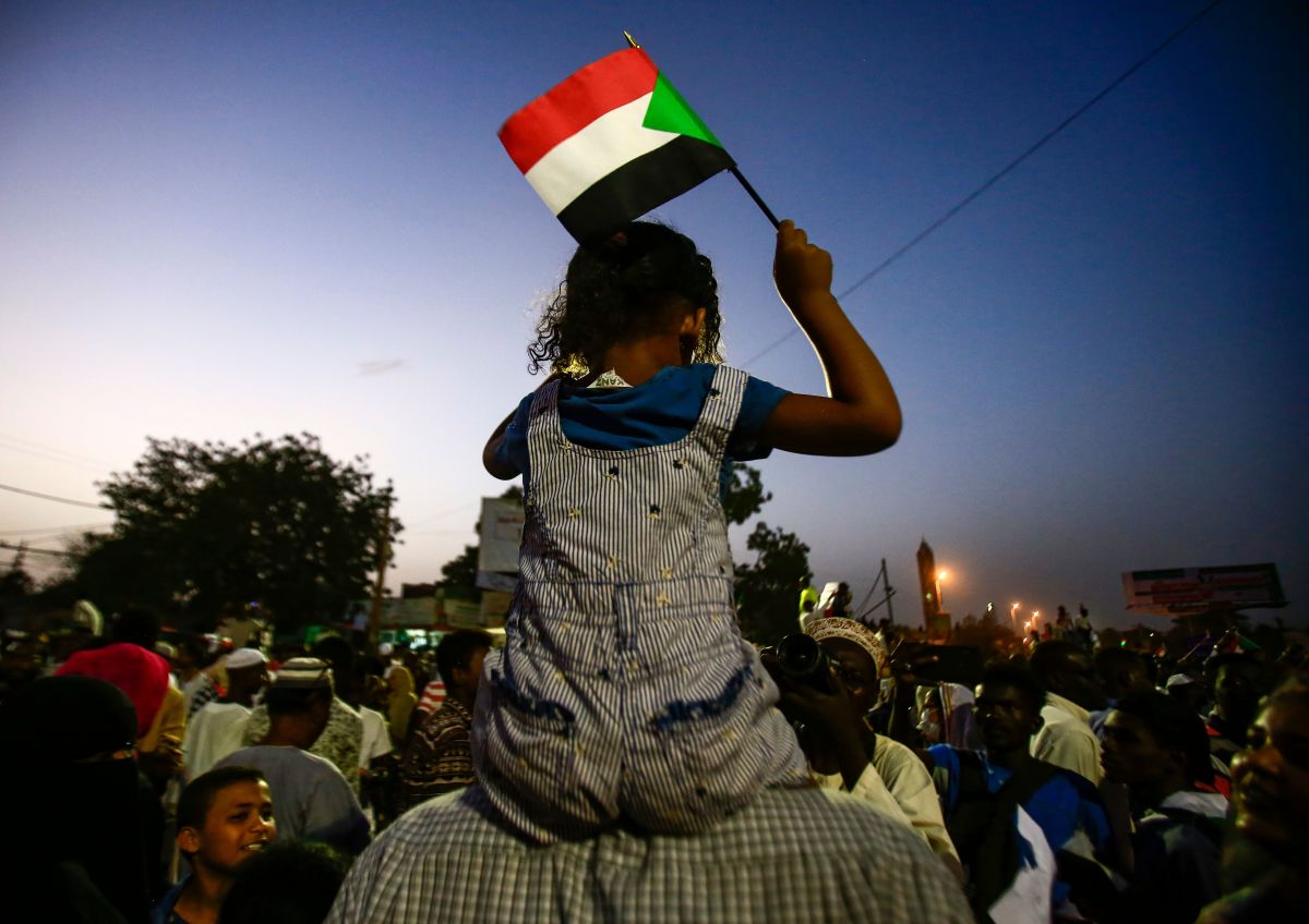 A Sudanese child waves a national flag as she sits atop the shoulders of a man during a late demonstration outside the army headquarters in the Sudanese capital Khartoum on April 12th, 2019. Protesters defied a night-time curfew to keep up four months of mass demonstrations.