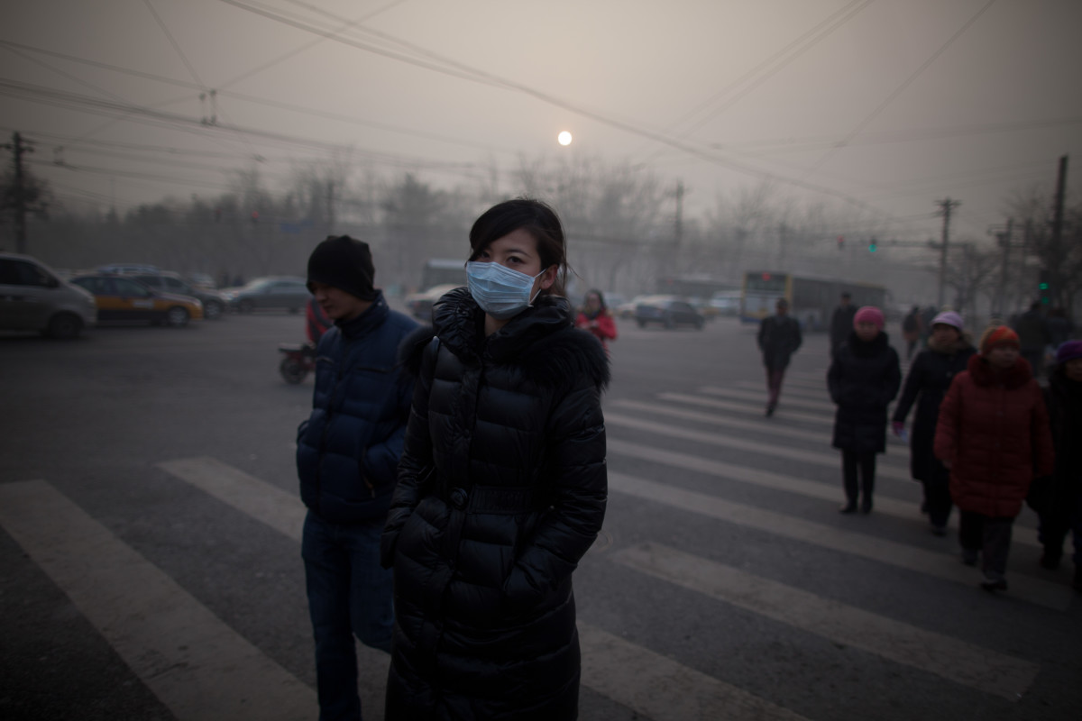 A woman wearing a mask crosses a road during severe pollution in Beijing on January 12th, 2013.