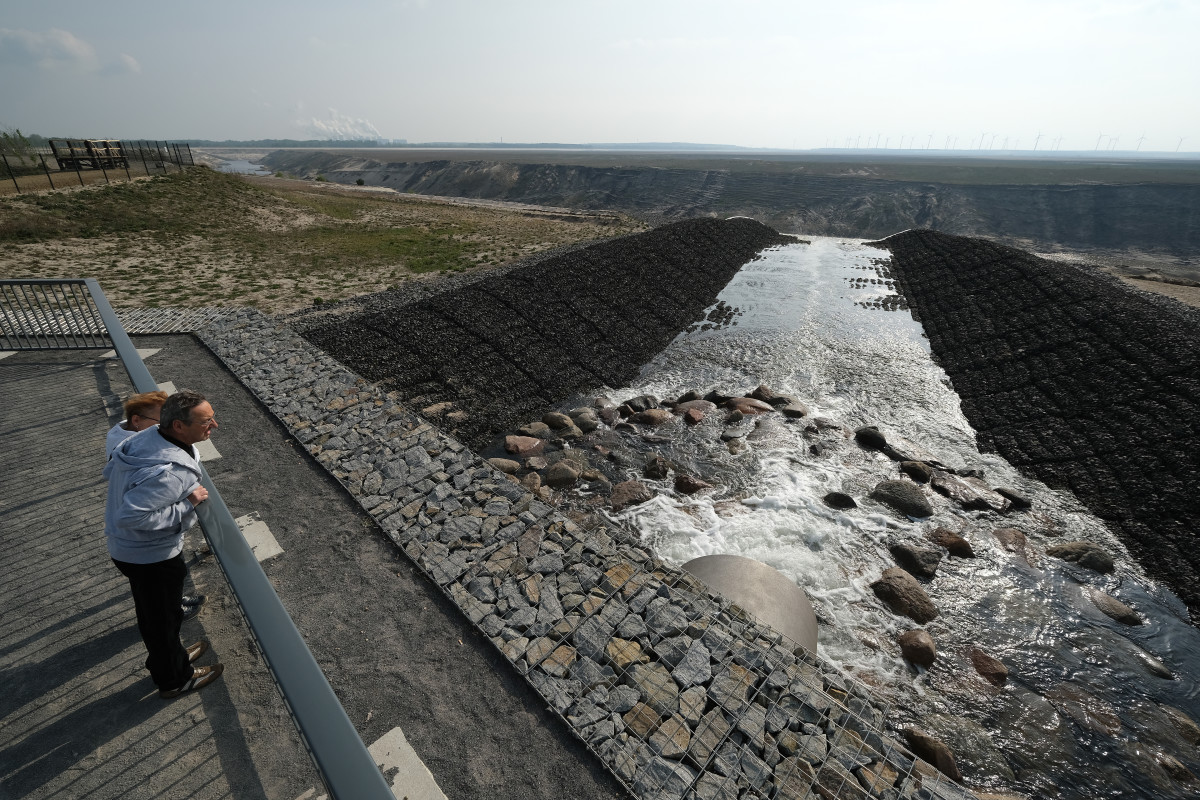 A couple watches as water gushes from a pipe into the former Cottbus Nord open-cast coal mine in order to create the Cottbuser Ostsee artificial lake on April 24th, 2019, near Cottbus, Germany. In the background, steam and exhaust rise from the Jaenschwalde power plant. The mine operated from 1975 until 2015 and fed coal to the Jaenschwalde plant. The former mine is now being flooded in its entirety to create a lake of 19 square kilometers for recreational use that local government planners hope will become a tourist destination and provide jobs. The flooding will take several years. The new Cottbuser Ostsee will be one of many artificial lakes in the region, some of which are already in use, that have been created from former coal mines.